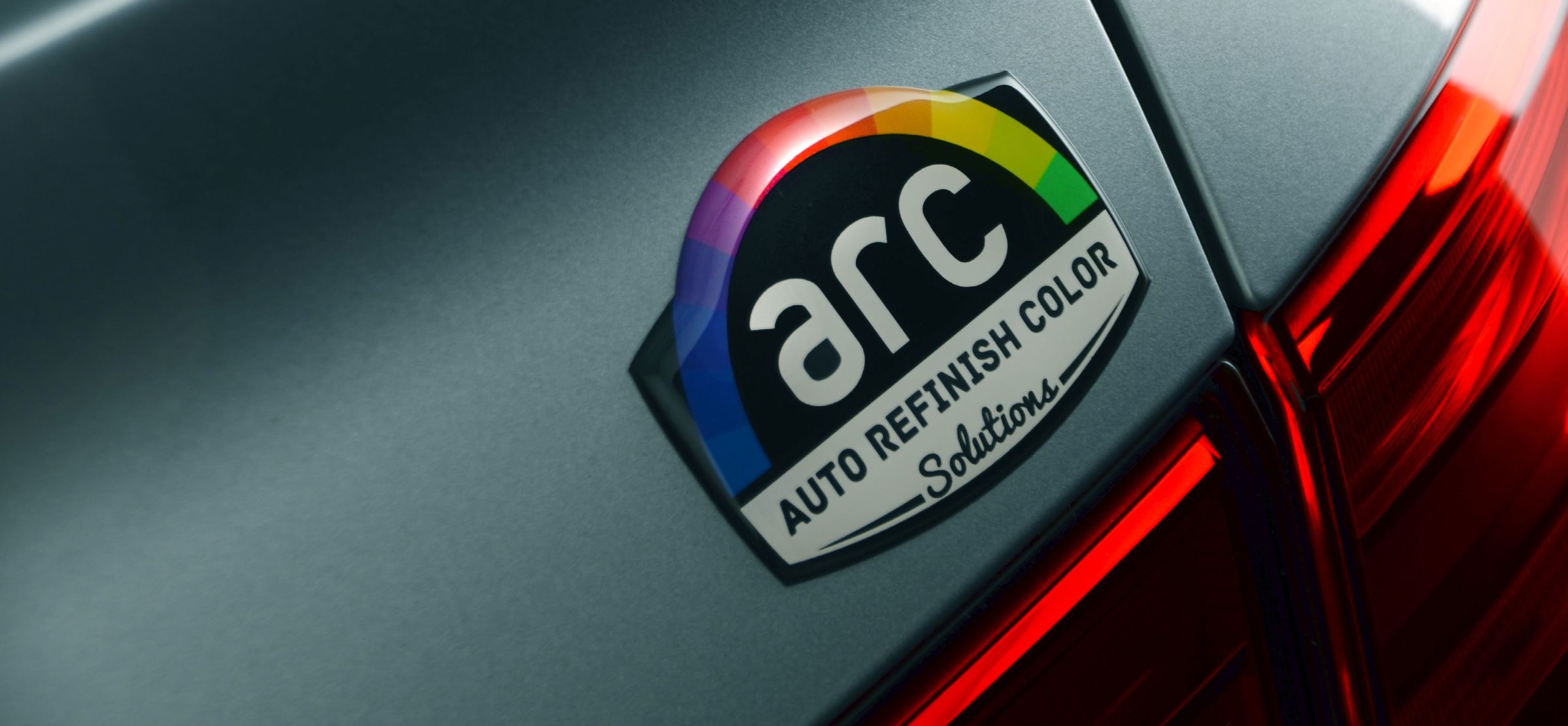 The ARC badge on the panel of a silver car, beside a red tail light